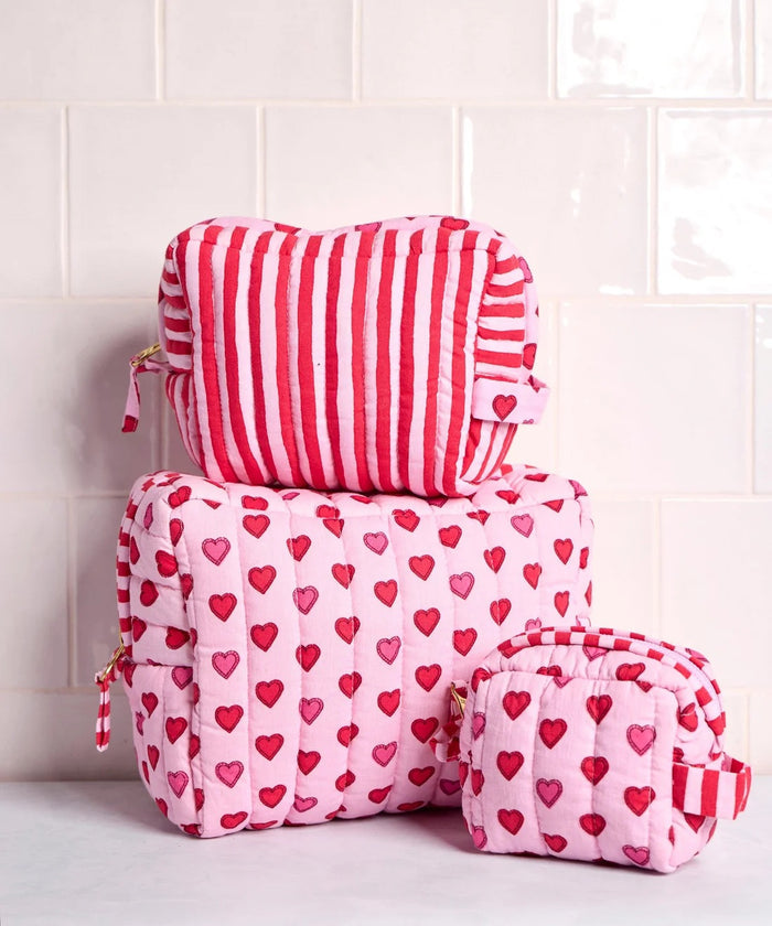 A person in a white ribbed sweater holds one of the charming heart pouches from the PRINTFRESH Mini Candy Hearts Three Pouch Set—a quilted cotton pouch from PRINTFRESH, finished in pink and adorned with red and pink hearts, plus a red-and-white striped tab.