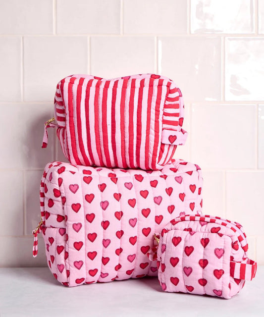 A person in a white ribbed sweater holds one of the charming heart pouches from the PRINTFRESH Mini Candy Hearts Three Pouch Set—a quilted cotton pouch from PRINTFRESH, finished in pink and adorned with red and pink hearts, plus a red-and-white striped tab.