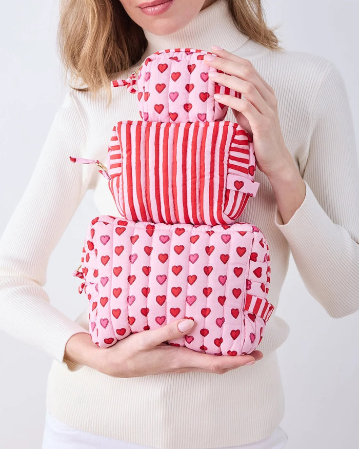 A person in a white ribbed sweater holds one of the charming heart pouches from the PRINTFRESH Mini Candy Hearts Three Pouch Set—a quilted cotton pouch from PRINTFRESH, finished in pink and adorned with red and pink hearts, plus a red-and-white striped tab.