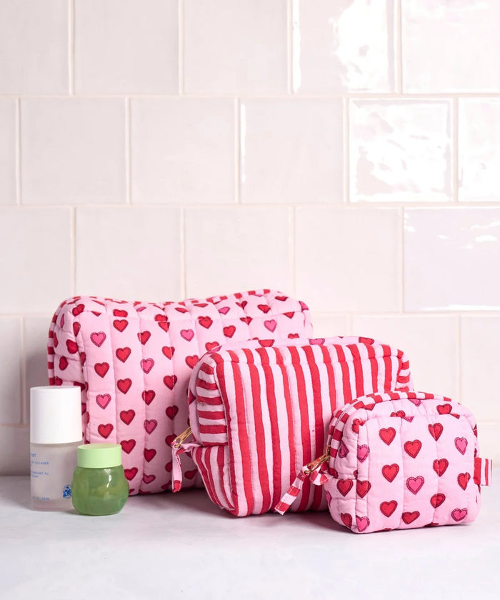 A person in a white ribbed sweater holds one of the charming heart pouches from the PRINTFRESH Mini Candy Hearts Three Pouch Set—a quilted cotton pouch from PRINTFRESH, finished in pink and adorned with red and pink hearts, plus a red-and-white striped tab.