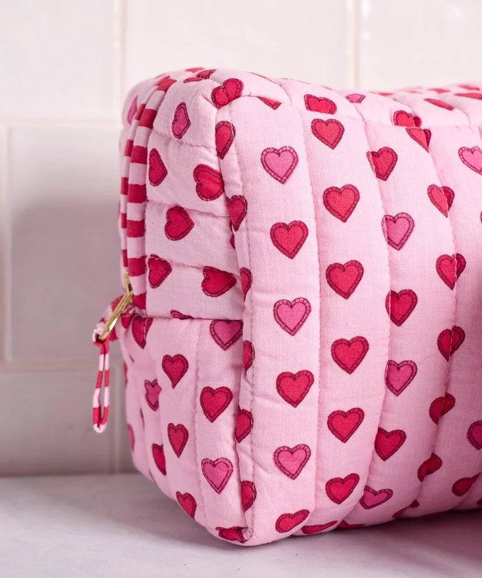 A person in a white ribbed sweater holds one of the charming heart pouches from the PRINTFRESH Mini Candy Hearts Three Pouch Set—a quilted cotton pouch from PRINTFRESH, finished in pink and adorned with red and pink hearts, plus a red-and-white striped tab.