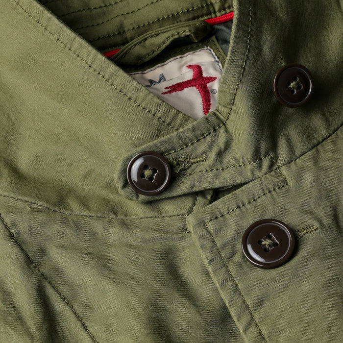 A person models the RELWEN Flyweight Flex Blazer in Burnt Olive over a blue and white checkered shirt with gray pants, hands in pockets, against a plain white background.