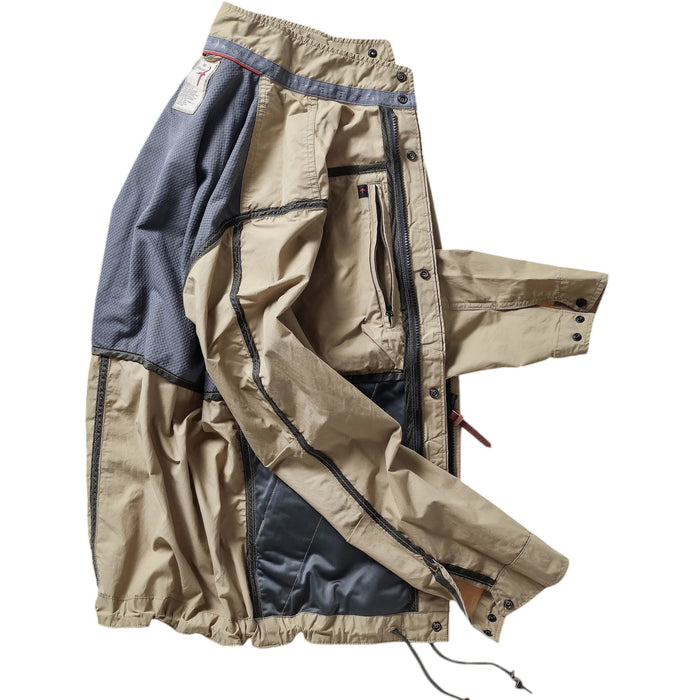 A person wearing the RELWEN Sailcloth Tanker in Desert Khaki stands on a wooden walkway, hands in pockets, with trees and sunlight in the background.