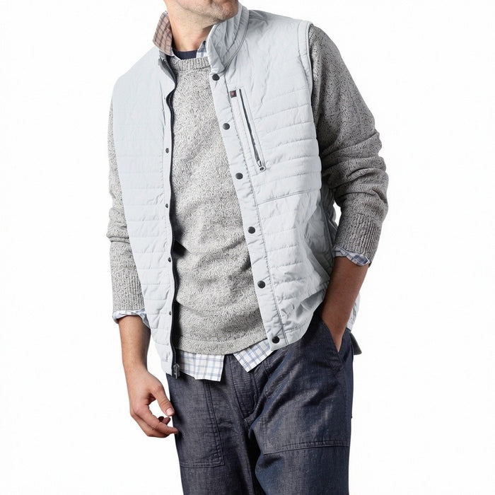 A person models the RELWEN - WINDZIP VEST IN GHOST GRAY over a gray sweater, plaid shirt, and dark blue jeans, standing with one hand in their pocket against a white background for extra layered warmth.