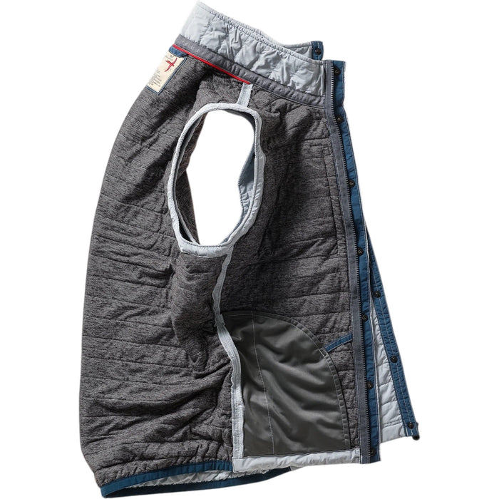 A person models the RELWEN - WINDZIP VEST IN GHOST GRAY over a gray sweater, plaid shirt, and dark blue jeans, standing with one hand in their pocket against a white background for extra layered warmth.