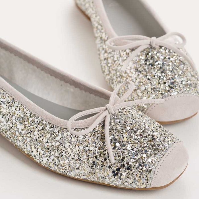 The REQINS HARMONY Sequin Ballerina Flat in Ice features a sparkling design with subtle pink trim and a small bow on the toe, shown from above against a plain light background.