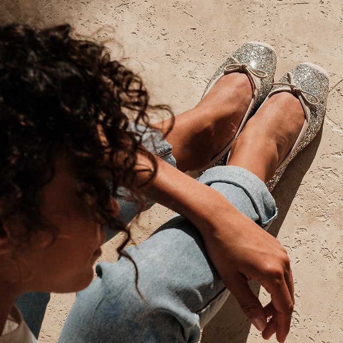 The REQINS HARMONY Sequin Ballerina Flat in Ice features a sparkling design with subtle pink trim and a small bow on the toe, shown from above against a plain light background.