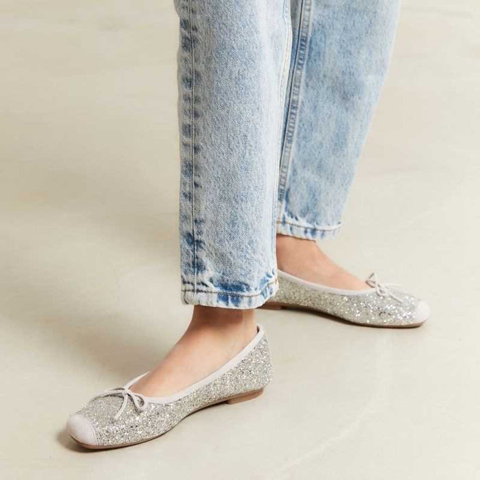 The REQINS HARMONY Sequin Ballerina Flat in Ice features a sparkling design with subtle pink trim and a small bow on the toe, shown from above against a plain light background.