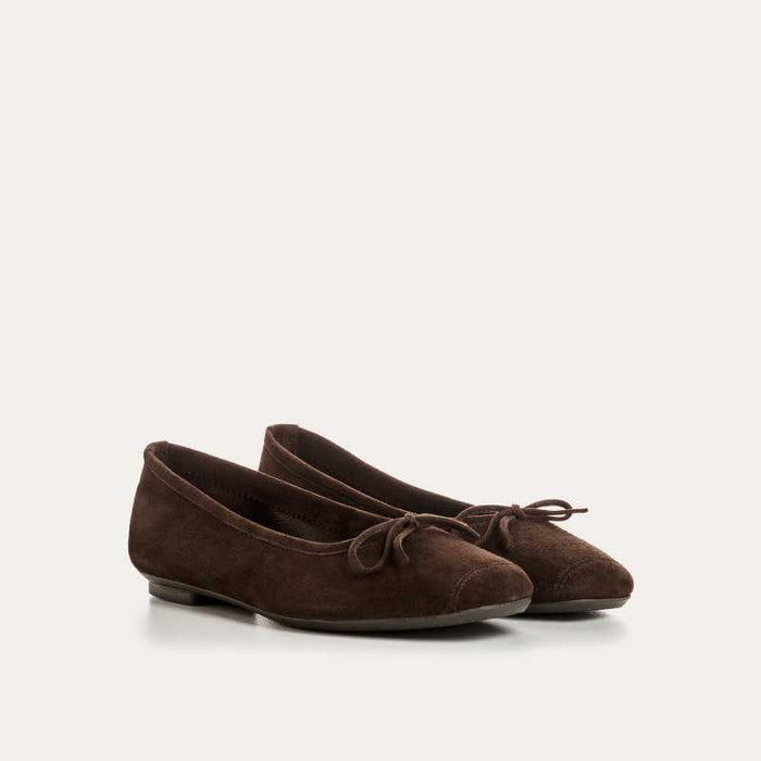 The REQINS HARMONY suede ballerina flats in Marron feature a dark brown finish and a small bow on the toe, shown in side profile against a plain light background—a timeless choice for any classic wardrobe.