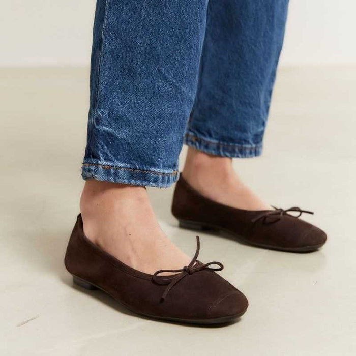 The REQINS HARMONY suede ballerina flats in Marron feature a dark brown finish and a small bow on the toe, shown in side profile against a plain light background—a timeless choice for any classic wardrobe.