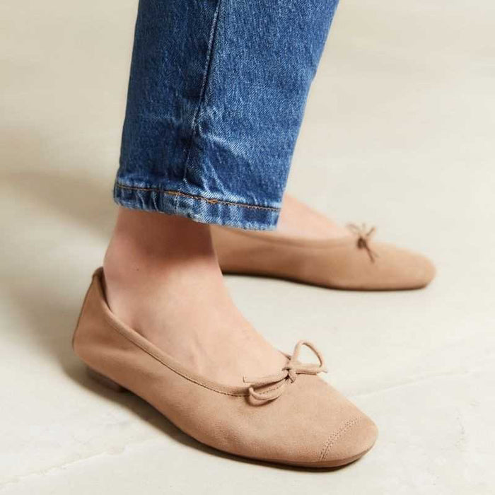 The REQINS - HARMONY SUEDE BALLERINA FLATS IN NATURAL by REQINS feature a small front bow and classic design, shown from the side against a plain light background—an essential wardrobe staple.