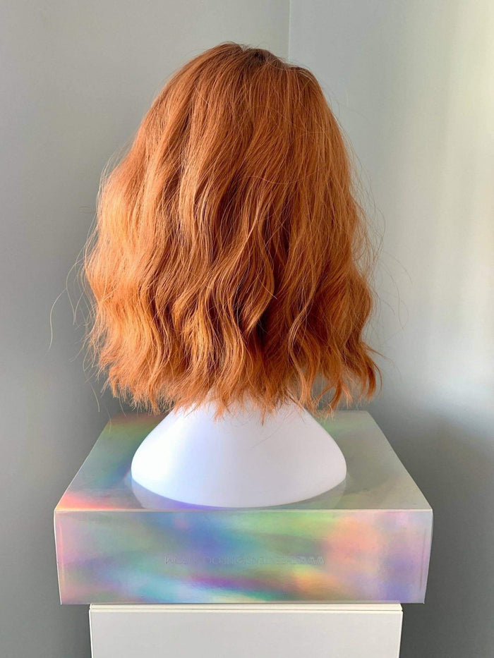 Rear view of a Robin Short Auburn Body Wave Wig with Bangs displayed on a stand, showcasing its wavy texture.