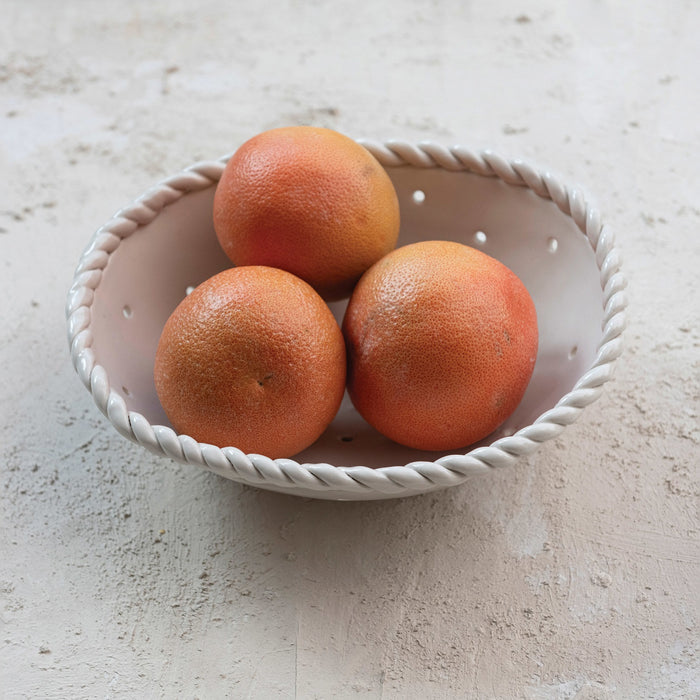 The CREATIVE COOP STONEWARE COLANDER WITH HAND TWISTED EDGE features small perforated holes and a braided rim, making it a perfect handcrafted addition to farmhouse style kitchens.