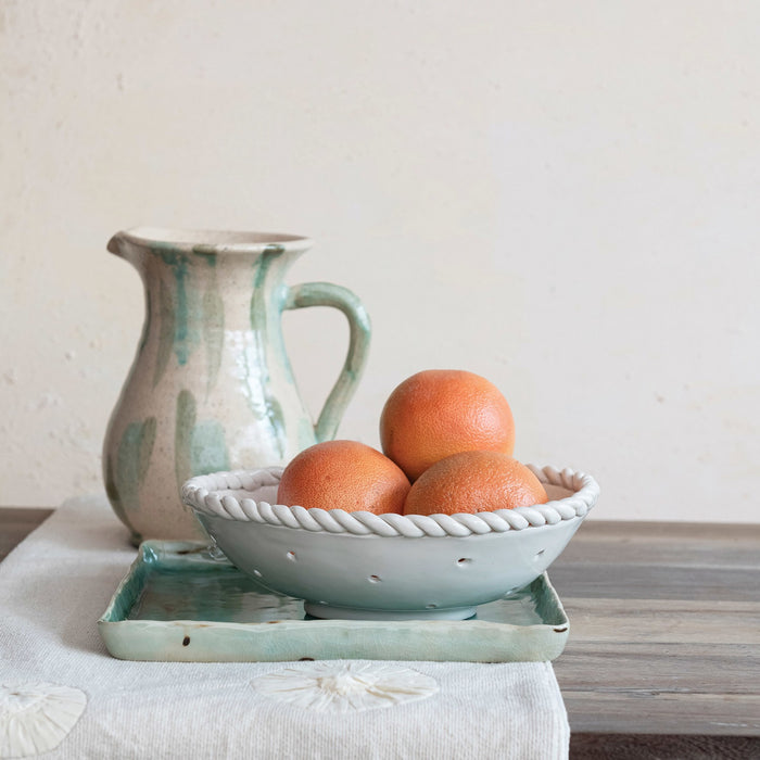 The CREATIVE COOP STONEWARE COLANDER WITH HAND TWISTED EDGE features small perforated holes and a braided rim, making it a perfect handcrafted addition to farmhouse style kitchens.