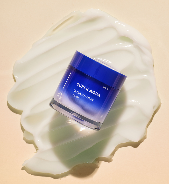 MISSHA Super Aqua Ultra Hyalron Cream jar in blue gradient packaging placed on a smooth layer of white cream texture, highlighting its hydrating and moisturizing formulation.