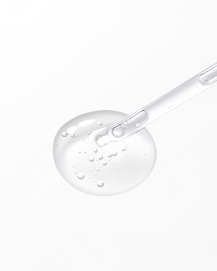 Close-up of a clear serum droplet with visible air bubbles and a glass dropper, showcasing the lightweight, hydrating texture of the skincare product.