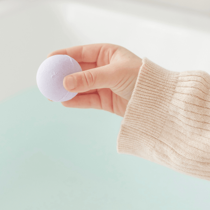 Hand holding a purple bath bomb against a light background