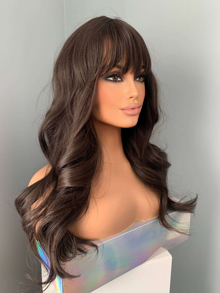 Tasha Long Dark Chocolate Brown Wig with Bangs displayed on a mannequin, featuring soft waves and a full fringe.