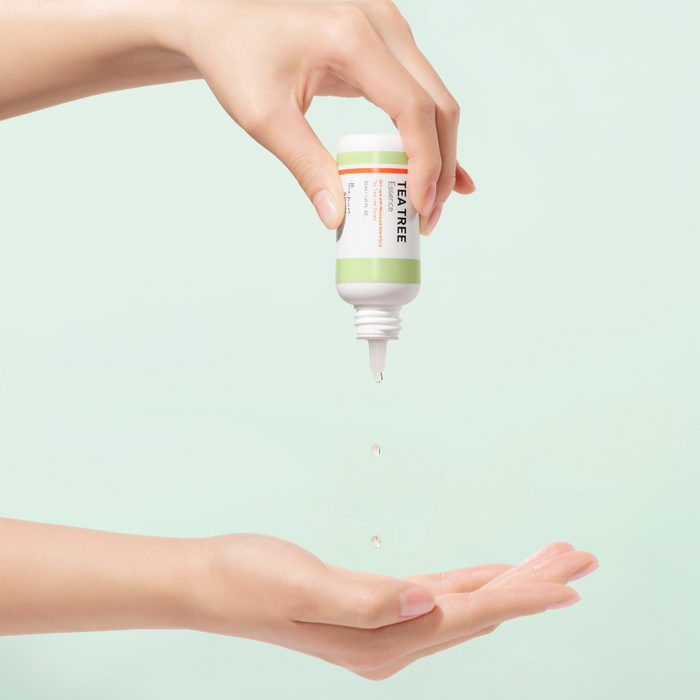 Hand holding a bottle of tea tree oil over another hand on a light green background