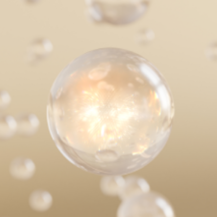 A close-up of a glowing, translucent golden droplet suspended in mid-air, representing a serum or essence texture with a radiant, luminous effect.