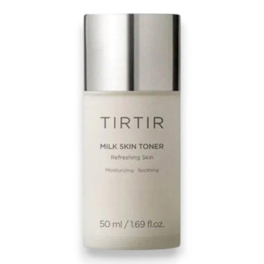 A hand holds a white bottle of TIRTIR - MILK SKIN TONER MINI, 50ML by KOSMIC KBEAUTY SKINCARE—a hydrating toner crafted to help you achieve glass skin. Key benefits are displayed with golden icons: soothing, gentle care, deep moisturization, anti-aging, and brightening. Featured ingredients like niacinamide are highlighted beside the icons. At the bottom, milk splashes accentuate the design.