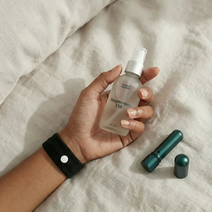 Hand holding a bottle of magnesium oil with a dropper on a beige fabric background