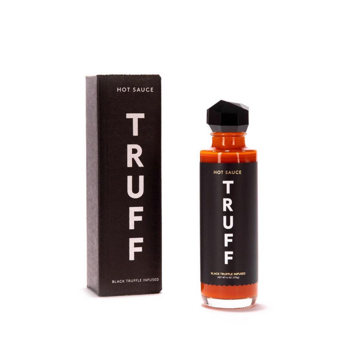 A bottle of TRUFF HOT SAUCE with a black label and geometric cap stands next to its matching box, both marked with "TRUFF - HOT SAUCE" in bold white letters.