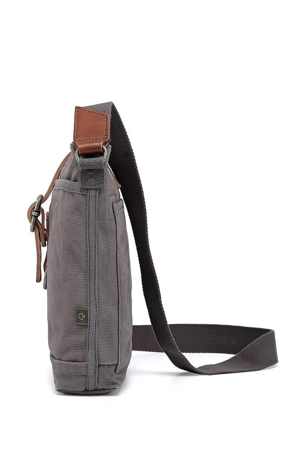 The TSD BRAND Forest Zip Crossbody Bag in Grey features a wide black strap, brown leather buckle accent, metal rivets, and a subtle side logo tag for a military-inspired look.