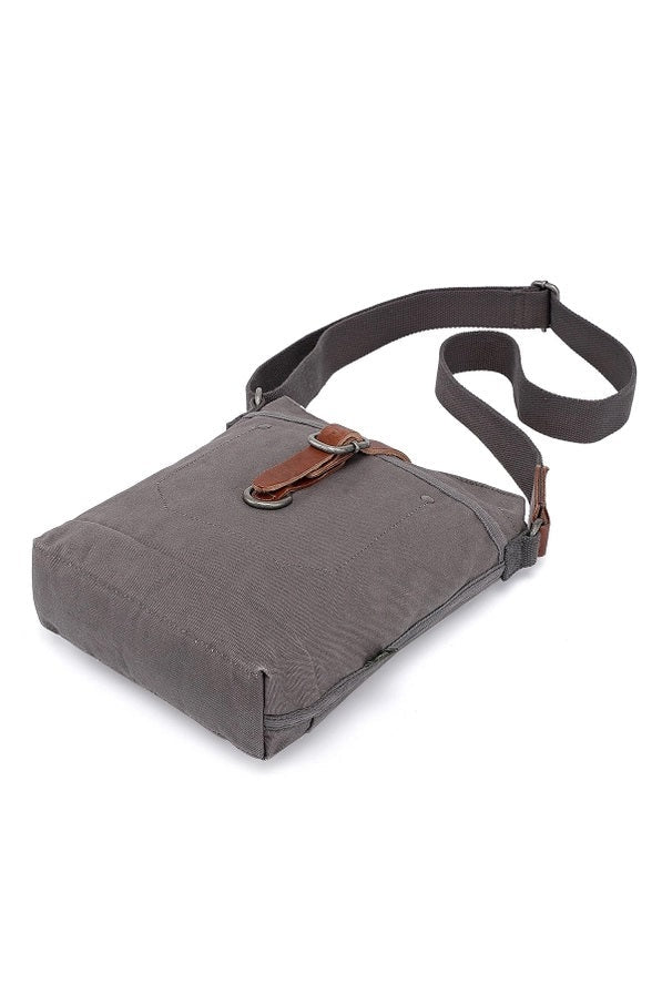 The TSD BRAND Forest Zip Crossbody Bag in Grey features a wide black strap, brown leather buckle accent, metal rivets, and a subtle side logo tag for a military-inspired look.