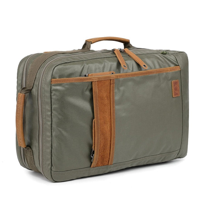 The TSD BRAND Madrone Coated Canvas Backpack in army green features brown leather accents, zippers, a top flap, side handles, metal rings, and a leather logo patch; shown lying flat to display these details.
