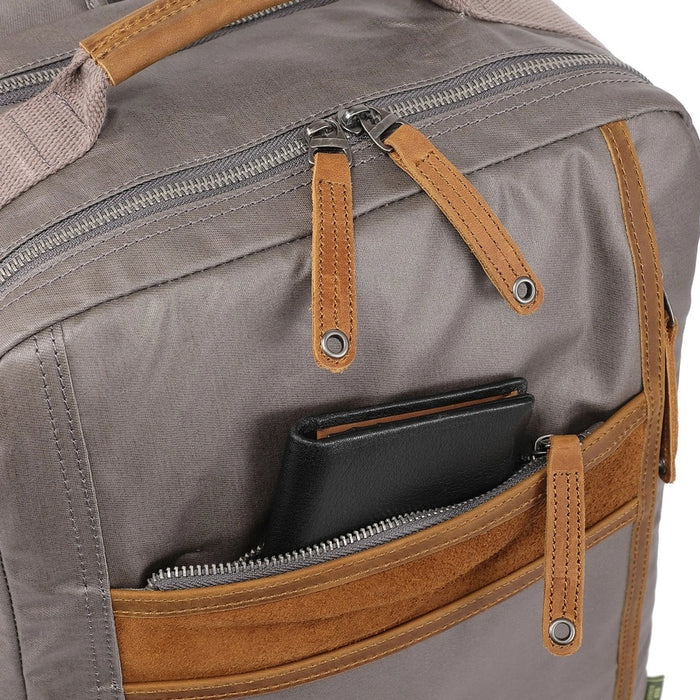 A close-up of the TSD BRAND - MADRONE Coated Canvas Backpack in Grey shows its brown leather accents and an unzipped front pocket with a black wallet partially visible inside.