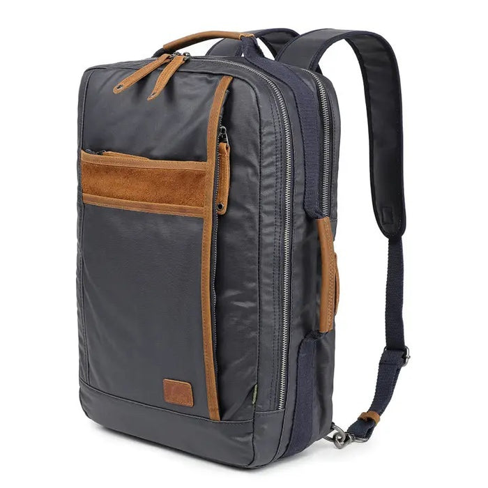 The TSD BRAND - MADRONE COATED CANVAS BACKPACK IN NAVY features brown leather accents, a spacious main compartment, a padded laptop sleeve with snap closure, and multiple zippered pockets on the inside flap.