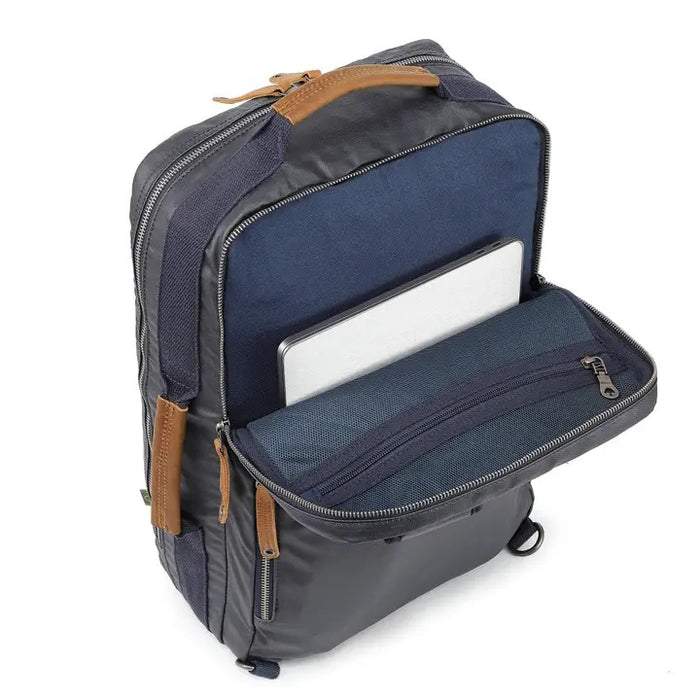 The TSD BRAND - MADRONE COATED CANVAS BACKPACK IN NAVY features brown leather accents, a spacious main compartment, a padded laptop sleeve with snap closure, and multiple zippered pockets on the inside flap.