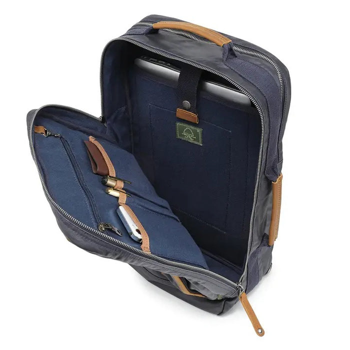 The TSD BRAND - MADRONE COATED CANVAS BACKPACK IN NAVY features brown leather accents, a spacious main compartment, a padded laptop sleeve with snap closure, and multiple zippered pockets on the inside flap.