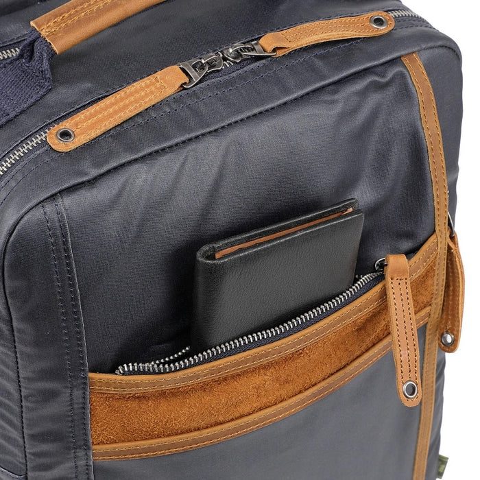The TSD BRAND - MADRONE COATED CANVAS BACKPACK IN NAVY features brown leather accents, a spacious main compartment, a padded laptop sleeve with snap closure, and multiple zippered pockets on the inside flap.