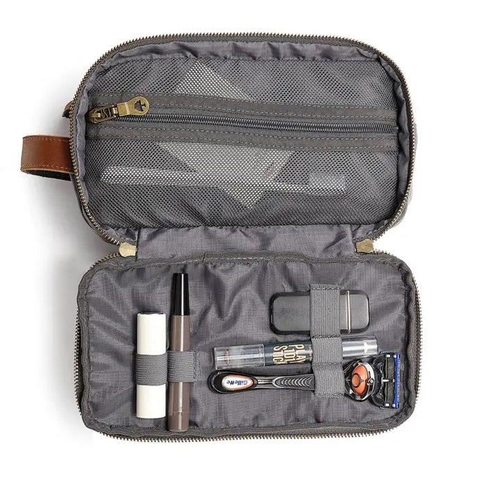 The TSD BRAND - Turtle Ridge Toiletry Bag in grey features waxed canvas, leather details, and a zip closure. It is open to show neatly organized travel essentials inside—bottles, a tube, a brush, and a white rectangular item.