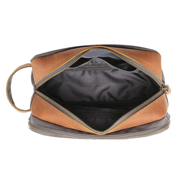 The TSD BRAND - Turtle Ridge Toiletry Bag in grey features waxed canvas, leather details, and a zip closure. It is open to show neatly organized travel essentials inside—bottles, a tube, a brush, and a white rectangular item.