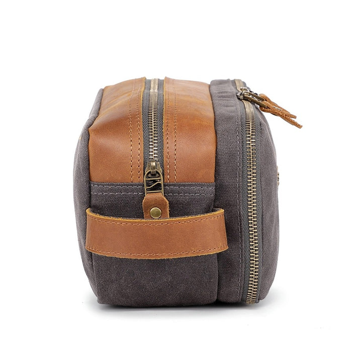 The TSD BRAND - Turtle Ridge Toiletry Bag in grey features waxed canvas, leather details, and a zip closure. It is open to show neatly organized travel essentials inside—bottles, a tube, a brush, and a white rectangular item.