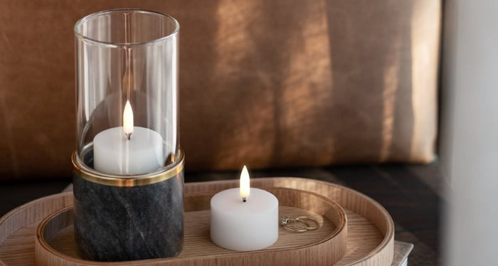 A compact, ivory UYUNI pillar candle (2x1.1) by PIFFANY with a glowing central flame, displayed against a simple white background.