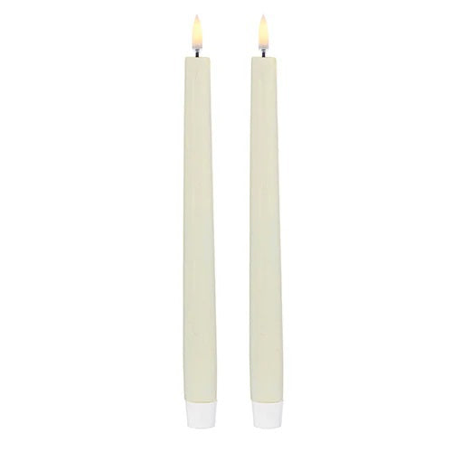 Two PIFFANY UYUNI Ivory Slim Taper Candles (1x12.6) with small yellow flames stand upright side by side against a plain white background, exuding timeless elegance.