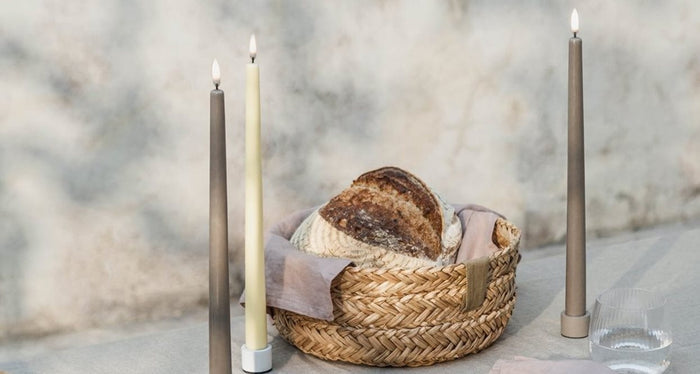 Two PIFFANY UYUNI Ivory Slim Taper Candles (1x12.6) with small yellow flames stand upright side by side against a plain white background, exuding timeless elegance.