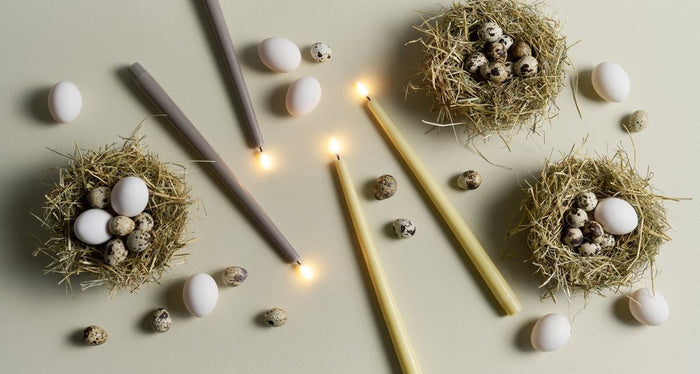 Two PIFFANY UYUNI Ivory Slim Taper Candles (1x12.6) with small yellow flames stand upright side by side against a plain white background, exuding timeless elegance.