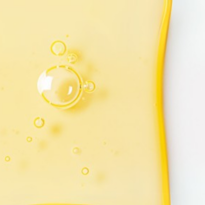 Close-up of a bright yellow serum texture with air bubbles, showing a glossy, smooth consistency and radiant finish.