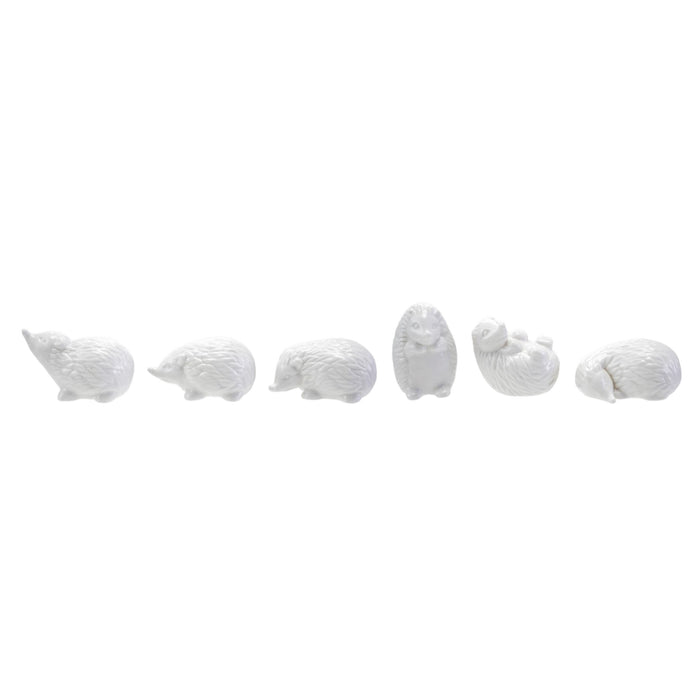 Six CREATIVE COOP WHITE STONEWARE HEDGEHOG figurines in different poses are arranged on and around three whitewashed cylindrical wooden pedestals, perfect for charming farmhouse decor. The background is plain white.