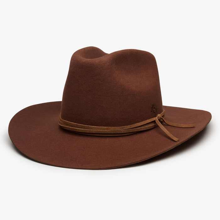 The WYETH Costa Cowboy Hat in Cinnamon features a wide brim, pinched crown, and thin suede trim tied in a bow. This adjustable hat by WYETH is shown on a white background.