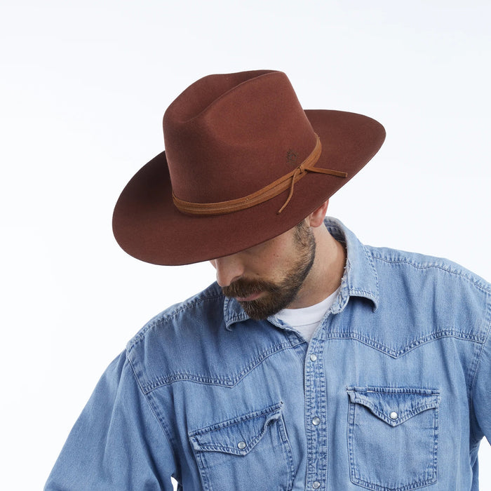 The WYETH Costa Cowboy Hat in Cinnamon features a wide brim, pinched crown, and thin suede trim tied in a bow. This adjustable hat by WYETH is shown on a white background.