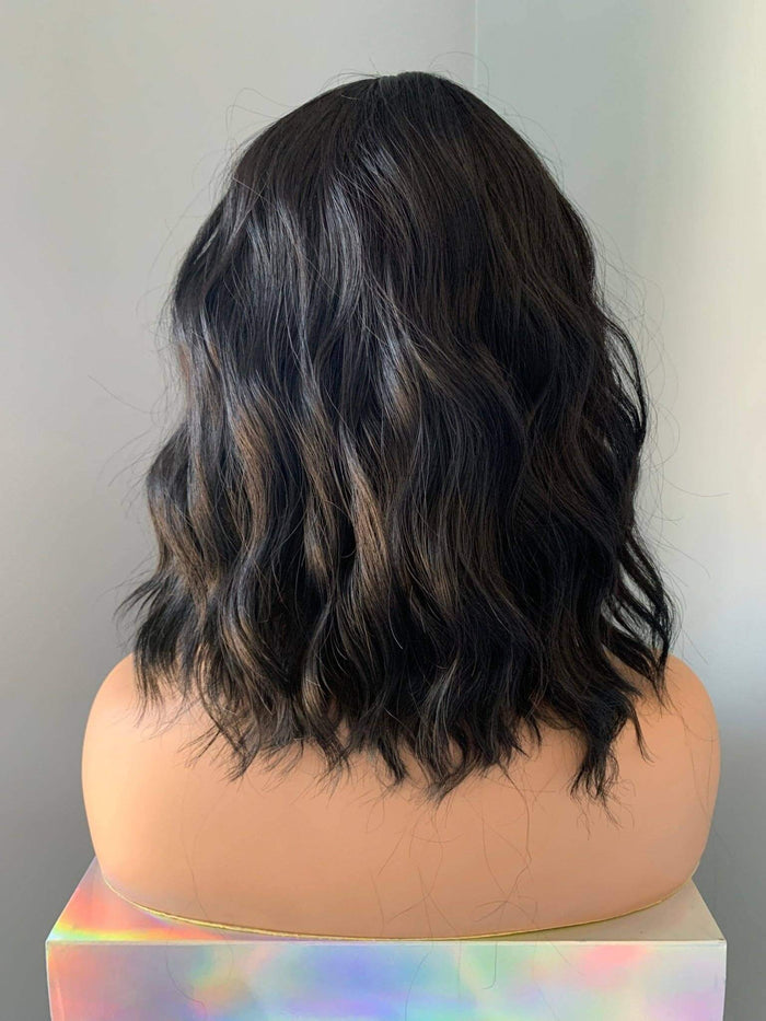 Black wavy wig on a mannequin head against a plain background
